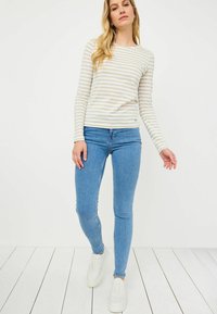 Maglietta a maniche lunghe con righe orizzontali beige e bianche, abbinata a jeans skinny azzurri e sneaker bianche. Design semplice e casual.