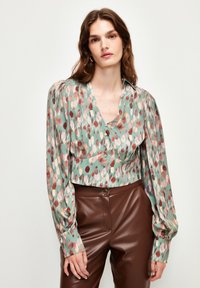 Blusa cropped con bottoni in tessuto verde menta, caratterizzata da colorati motivi a pois astratti. Maniche a palloncino e scollatura a V profonda.