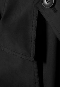 Materiale del cappotto trench nero con una superficie liscia. Presenta un ampio collo, hardware con bottoni e dettagli di cucitura visibili. Nessun motivo.