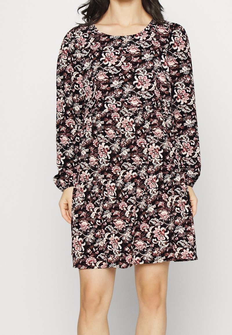 Kukkamekko mustana, jossa on pinkkejä ja valkoisia kuvioita, pitkät hihat, pyöreä kaula-aukko ja kerätty vyötärö. Pehmeä kangas, joka on rento istuvuus.