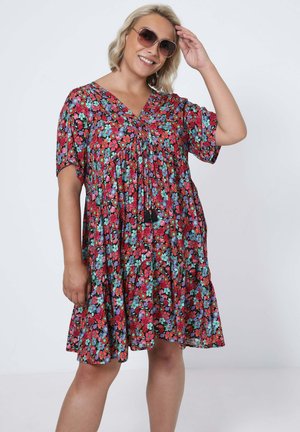 Robe fleurie rouge avec des fleurs multicolores, à manches courtes, décolleté en V et détails froncés. Comprend des accents de pompons près du décolleté.