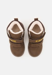 Bottes en daim brun avec doublure en peluche, bandes velcro et logo jaune. Forme de bout arrondi et détails de couture contrastants.