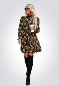 Abito nero floreale con motivi gialli, Collo alto, vita cinquecento, e maniche lunghe. Indossato con stivali neri fino alla coscia, con una tazza di caffè in mano.
