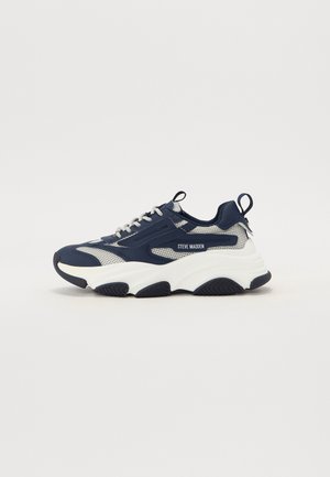 Gruby sneaker Steve Madden w granatowym i szarym mesh z grubą białą podeszwą i paskami do zakładania na pięcie i języku.