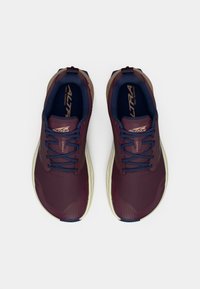 Bordowe buty do biegania z teksturowaną siateczką na górze, granatowymi akcentami i beżową podeszwą. Posiada okrągłe sznurówki i wzmocnioną piętę dla wsparcia.
