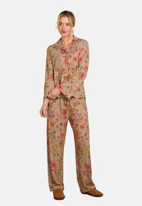 Beige pyjamastel met bloemenpatroon, met lange mouwen en losse broek. Borduursel met roze, rode en gele bloemen. Zachte stof textuur.