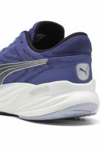 Scarpa da corsa viola con tomaia in tessuto texturizzato, dettagli argentati, bordi neri e una suola bianca spessa con un design curvo.