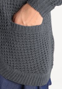 Stickad grå tröja med ett strukturerat mönster, utrustad med en stor sidoficka och ribbade ärmslut och fåll. Designad för en lös passform.