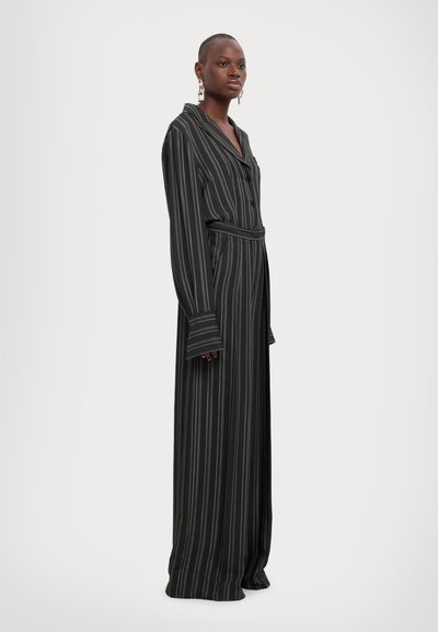 Rochie cu dungi negre, cu mâneci lungi, guler în formă de V, închidere cu nasturi și talie evidențiată cu un brâu. Prezintă un design fluid și o siluetă lungă până la podea.