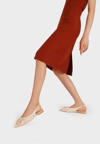 Scarpe slingback beige con punta affusolata, texture intrecciata e un elegante dettaglio a fibbia. Suola piatta e design aperto sul retro per favorire la traspirabilità.