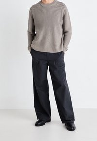 Grå ribbet sweater med geometriske mønstre, parret med løstsiddende sorte cargobukser. Solide sorte støvler fuldender outfittet.