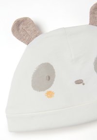 Panda-motivierte Babykappe aus weichem, weißem Stoff, mit grauen Gesichtselementen, orangefarbenen Akzenten und beigen Ohren, die oben herausragen.