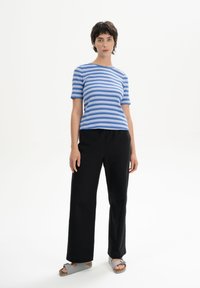 Blue and white striped t-shirt with short sleeves, paired with loose black pants and grey sandals, set against a plain white background.