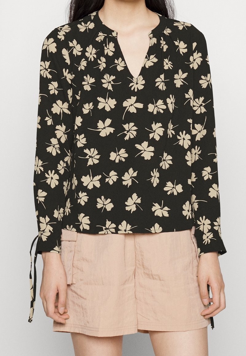 Blusa nera a maniche lunghe con motivo floreale bianco, scollatura a V e dettagli a fiocco ai polsi. Abbinata a pantaloni shorts rosa chiaro.