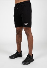 Zwarte sportshorts van zachte stof, met een elastische tailleband, zijzakken en een Gorilla Wear-logo in het wit gedrukt.