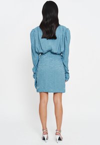 Jasnoniebieska sukienka z bufkami i teksturowanym materiałem. Posiada dopasowaną talię i d�ługość do kolan. Stylizowana z sandałami na wysokim obcasie.