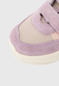 Μύτη αθλητικού παπουτσιού σε μπεζ και λεβαντί σουέντ με ύφασμα από δίχτυ και ραμμένες λεπτομέρειες σε εκρού σόλα πάνω σε λευκό φόντο.