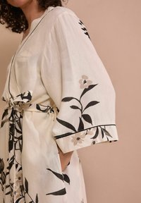 Jasno kolorowy kimono z kwiatowym wzorem w odcieniach czerni i beżu. Posiada paski do wiązania, luźne rękawy oraz kontrastowe wykończenia przy mankietach.