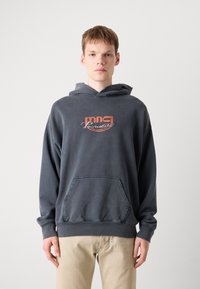 Sudadera gris con bolsillo delantero y capucha con cordón. Cuenta con un logo impreso en naranja y blanco. Material suave y texturizado. Ajuste casual.