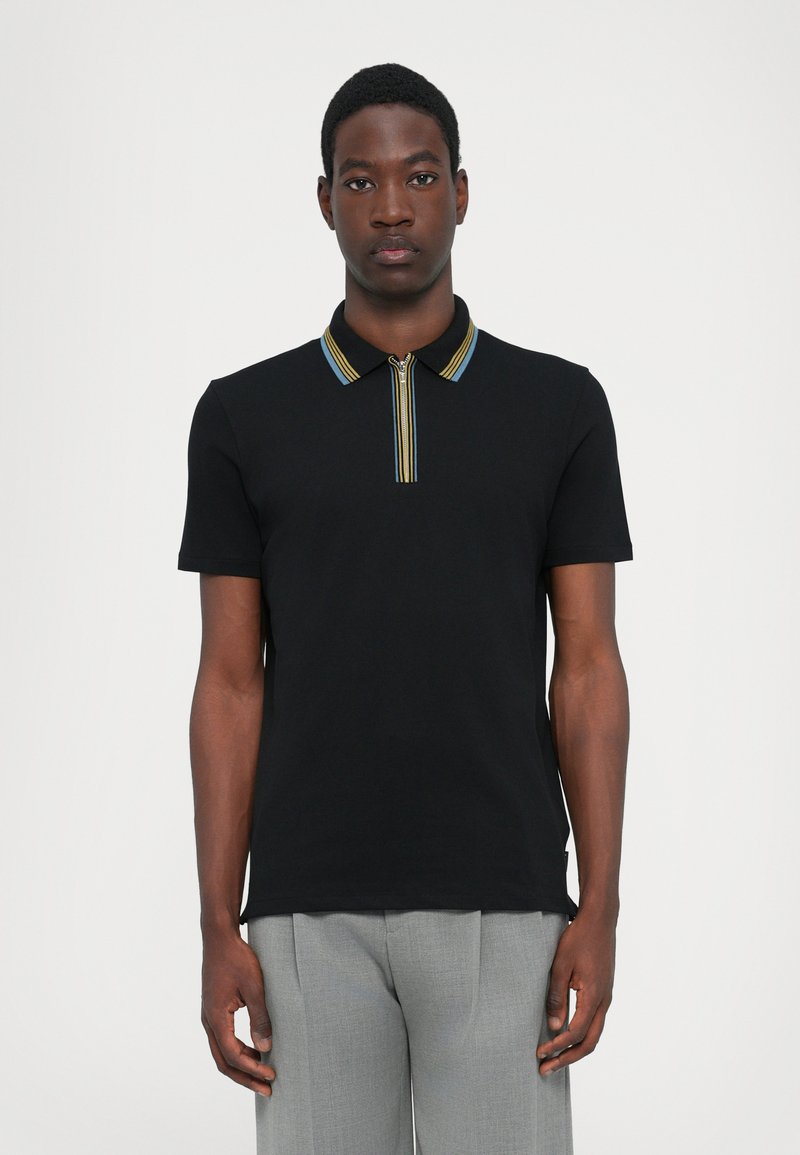 Camisa polo negra de manga corta, con cuello con cremallera y ribete a rayas multicolores. Tejido de algodón texturizado. Diseño ajustado.