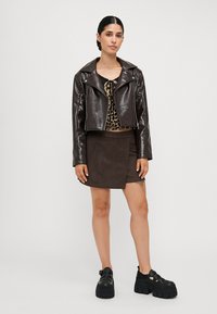 Brun faux skinnjakke med brede slag, kombinert med en svart leopardmønstret topp og et brunt suedeminiskjørt. Svarte platåsko.