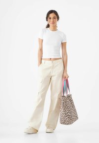 T-shirt blanc ajusté, pantalon cargo beige avec poches, et un sac à imprimé léopard avec des anses rayées rose et bleu. Look décontracté avec des textures variées.