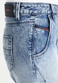 Vaalean siniset happopesutetut farkut, joissa on etu- ja takataskut, näkyvät saumat, vyölenkit ja musta etiketti, jossa on punainen "Diesel"-brändi.