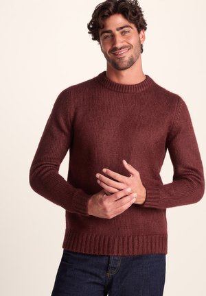 Burgundy knit sweater with a round neck, ribbed cuffs and hem, featuring a textured finish and a relaxed fit. Worn with dark jeans.