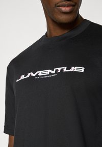 Μαύρο βαμβακερό κοντομάνικο μπλουζάκι με εκτυπωμένο λογότυπο «JUVENTUS» σε λευκό και ροζ, με στρογγυλή λαιμόκοψη και απαλό ύφασμα.