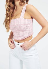 Top corto a quadri rosa con scollatura quadrata e orlo frangiato, realizzato in tessuto testurizzato. Abbinato a jeans bianchi a vita alta.