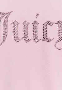 Ljusrosa velourtröja med ordet "Juicy" i glittrande rhinestones. Designen har en djärv, stiliserad font och en glänsande textur.