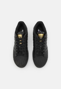 Svarta sneakers i läder med texturerad tå, platta snören och gulddetaljer. Har tre ränder på sidorna och vadderade kragar.