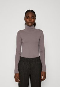 Långärmad polotröja i dämpad lavendel, tillverkad av mjukt tyg, ihop med svarta byxor med smala ränder. Enkelt design och åtsittande silhuett.