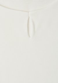 Close-up of a white fabric with a small vertical keyhole cutout and seam detailing near the top center.