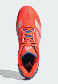 Jasně oranžová sportovní bota s bílými pruhy, modrým vnitřkem a oranžovými tkaničkami, zobrazena z pohledu shora.