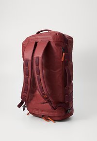 Sac de sport rouge avec deux sangles réglables, une poignée supérieure, une fermeture éclair latérale et des accents orange. Fabriqué en tissu durable et lisse. Forme arrondie.