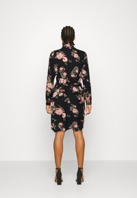 Abito nero con maniche lunghe, motivo floreale caratterizzato da rose rosa. Ha una vita aderente e arriva sopra il ginocchio, abbinato a scarpe con tacco a blocco.