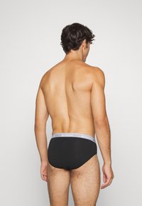 Schwarze Unterhose mit grauem SLOGGI-Bund, glattes Material, enganliegendes Design und minimale Nähte. Ansicht von hinten, die den Bund und den Schnitt zeigt.