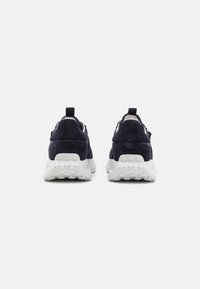 Granatowe zamszowe sneakersy z teksturowaną białą gumową podeszwą. Posiadają pętelkę przy pięcie oraz minimalistyczny design, podkreślający funkcjonalność i komfort.