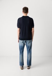 Polo à manches courtes bleu marine avec col, bordure blanche aux manches, associé à un jean bleu clair et des baskets beige.