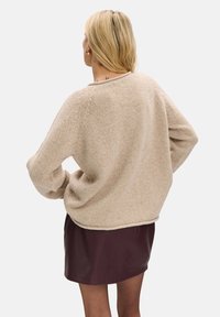 Beżowy dzianinowy sweter z długimi rękawami, teksturowaną tkaniną i krótkim krojem, połączony z ciemnoczerwoną skórzaną spódnicą.