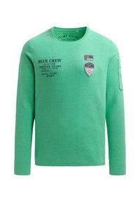 Grünes Langarm-T-Shirt aus einem strukturierten Stoff. Verfügt über Text und Patches auf der Vorderseite, einen runden Ausschnitt und umgeschlagene Ärmel.