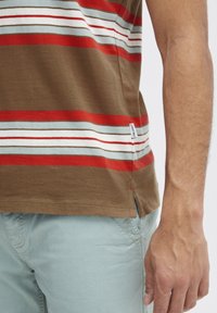 T-shirt rayé marron avec des rayures horizontales rouges, bleues et blanches ; en coton doux, doté de fentes latérales et d'une étiquette de marque sur l'ourlet.