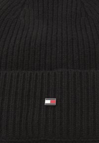 Beanie de tricot cu iarnă, negru, cu o etichetă rectangulă mică în roșu, alb și albastru. Material cald; textură groasă; se așază bine.