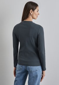 Grijze geribbelde langokkige shirt met ronde hals, gecombineerd met lichtblauwe denim jeans. Soepele textuur en nauwsluitend ontwerpdetail.