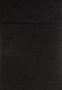 Črna bombažna nogavica z rebrasto teksturo na vrhu, gladkim telesom in brez vidnih vzorcev ali poudarkov. Preprost in funkcionalen dizajn.