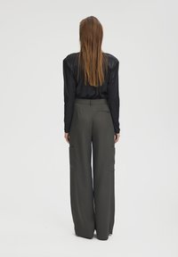 Maglietta nera a maniche lunghe e pantaloni a gamba larga a vita alta in grigio scuro, dotati di tasche laterali e con una finitura di tessuto testurizzato.