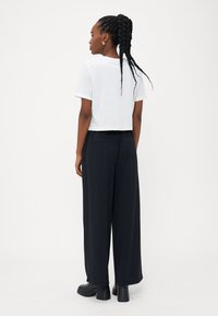 T-shirt bianco cropped abbinato a pantaloni neri larghi. I pantaloni presentano una vestibilità rilassata e tasche discrete. Scarpe nere con plateau completano il look.