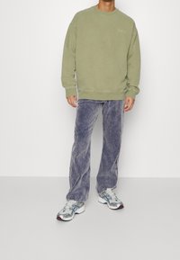 Olivově zelená mikina s ribováním na manžetách, spojená se světle fialovými kordovými kalhotami. Obuv má stříbrné akcenty a retro design.