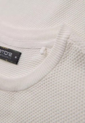 Biała, fakturowana dzianina z ribbówym dekoltem. Posiada małą metkę z nazwą marki i rozmiarem. Zbliżenie na detale koszulki.